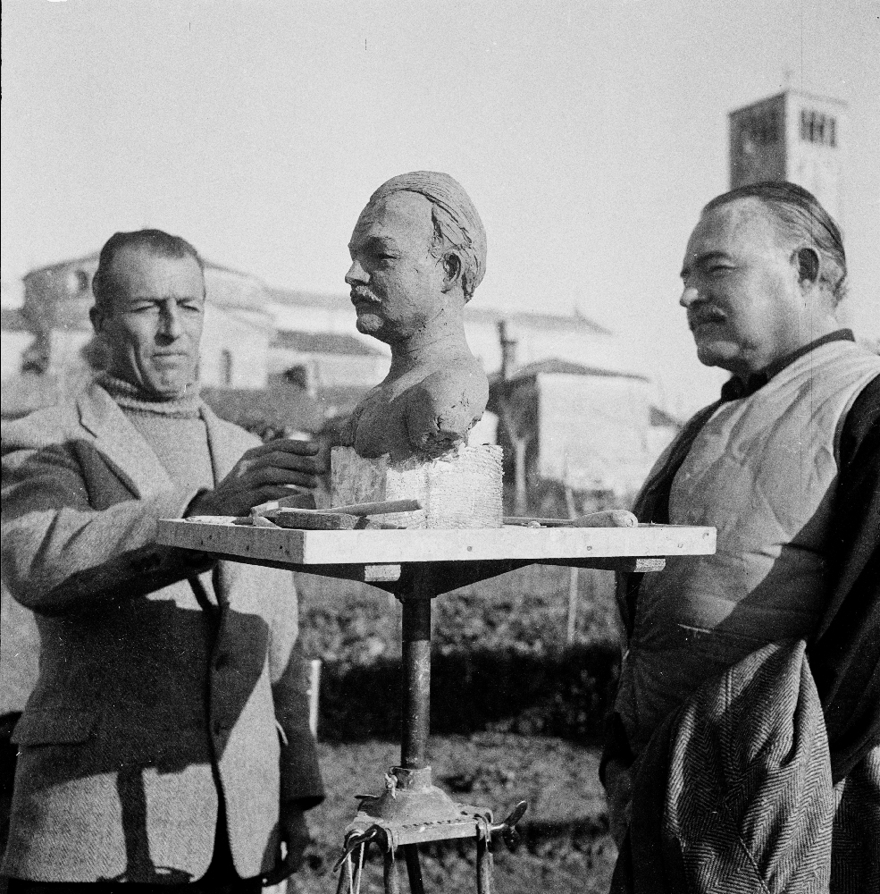 EH2812S December 1948 Ernest Hemingway with unidentified man and a sculpture of Hemingway's bust. Torcello Island, Venice, Italy. Copyright: Ernest Hemingway Collection at the John F. Kennedy Presidential Library and Museum, Boston.