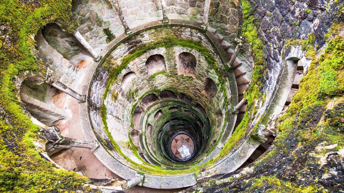 The mysterious spiral staircase of the Initiation Well at Quinta da Regaleira in Sintra, Portugal, with mossy stones and light filtering from above.